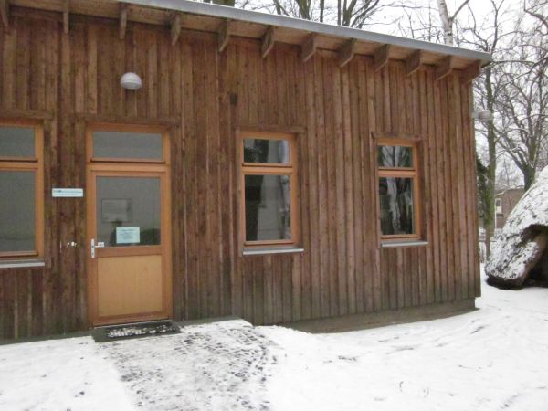 Ein Nebengebäude aus Holz ist zu sehen. Es liegt Schnee.