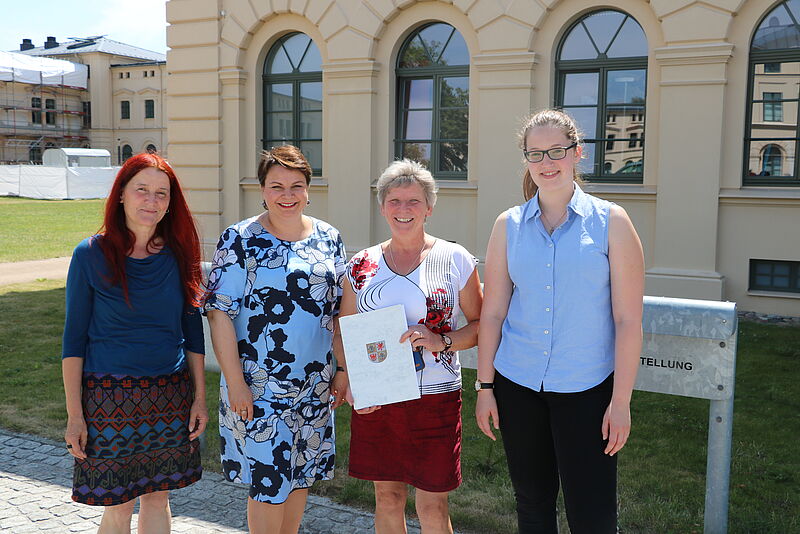 Vor dem Schweriner Schloss überreicht die Sozialministerin von Melckenburg-Vorpommern, Stefanie Drese, drei Kolleg*innen der LKJ MV symbolisch den Förderbescheid. 