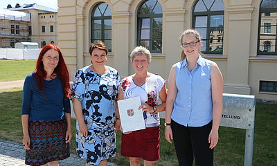 Vor dem Schweriner Schloss überreicht die Sozialministerin von Melckenburg-Vorpommern, Stefanie Drese, drei Kolleg*innen der LKJ MV symbolisch den Förderbescheid. 
