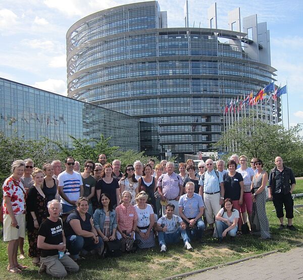 Eine Gruppe von älteren und jüngeren Menschen steht vor dem Europaparlamentsgebäude in Straßburg.