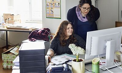 Zwei Personen schauen konzentriert auf einen Bildschirm eines Computers. Sie sitzen in einem Büro.
