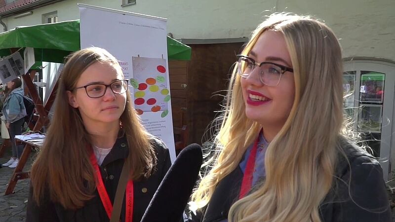 Zwei junge, weiße Frauen mit Brillen werden interviewt. Standbild aus dem Youtube-Video Auf- und Abgesang, das oben verlinkt ist. 
